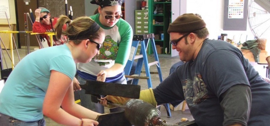 Students Brandi Hunt, left, and Tori Niemeier help instructor Brian Alloway work a piece of glass during class at Hocking College. (Arian Smedley/The Athens Messenger)