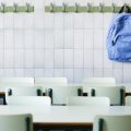 A row of desks in a classroom with a backpack hanging up on the back wall