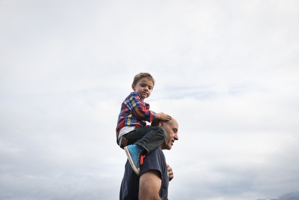 Lyle holds his adopted son Levi, 3, on his shoulders to watch Gabe, his biological son, race in his motocross competition at Fast Traxx Racing.
