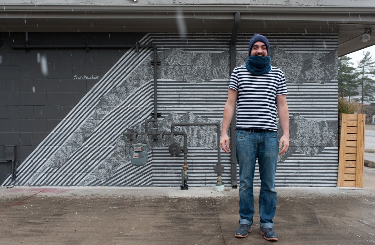Andrew Clavin stands in front of the finished chalk mural at OMG! Rotisserie on Columbus Rd. The mural took over twelve hours to complete using only tape and white chalk. (Mark Clavin/WOUB)  