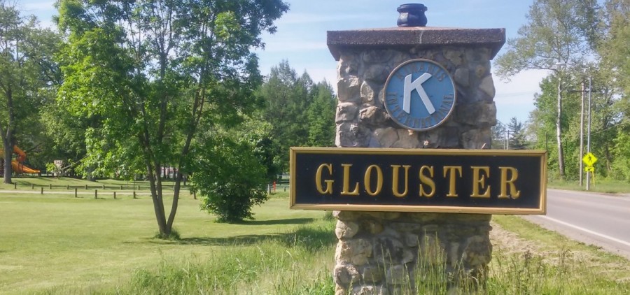 A sign for the town of Glouster mounted on stone and mortar pillar by the road