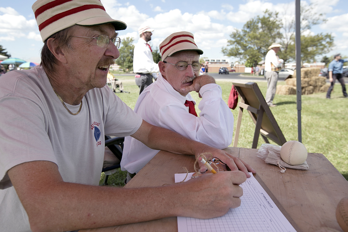 Larry Hoffman, left, and Duane Koons, right, took a break from playing in the Ohio Cup in Columbus on Saturday to work as tally keepers. Both men are on the Ohio Village Muffins team, which hosts the Ohio Cup each year so that dozens of other vintage baseball teams from all over the United States can play against one another. (WOUB/Jennifer Coombes)
