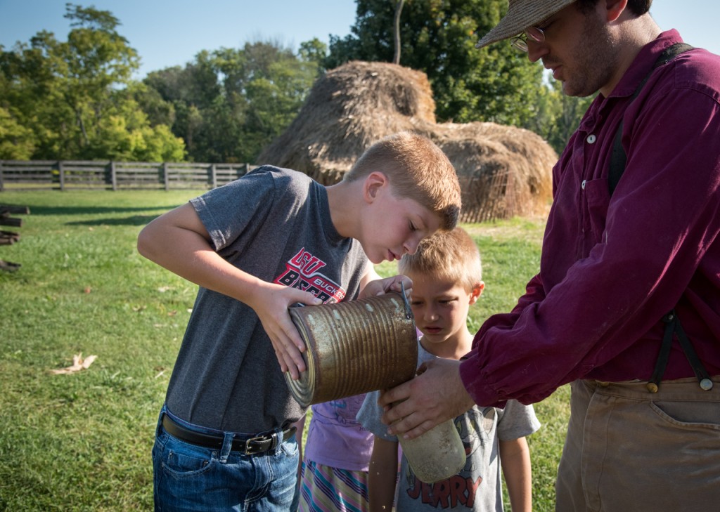 Max Harshen (left) pouring food into a feeder for ducklings while, Peter (last name withheld) (middle) watches and Jeremy Angstadt holds the container steady for Harshen as an activity of the Morning Chores Program at at Slate Run Living Historical Farm in Canal Winchester, Ohio, on September 10, 2016. (WOUB/ Carolyn Rogers)