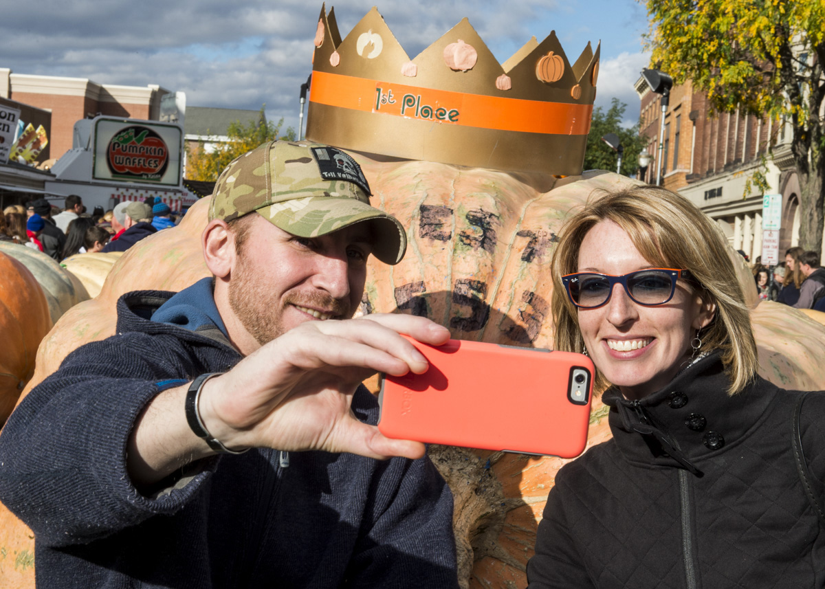 Dan Haywood, left, and Gretchen Kuhn, right, from Oakwood, Ohio, take a selfie in front of the winning pumpkin in size at the Circleville Pumpkin Show on October 22, 2016. (Robert McGraw/WOUB)