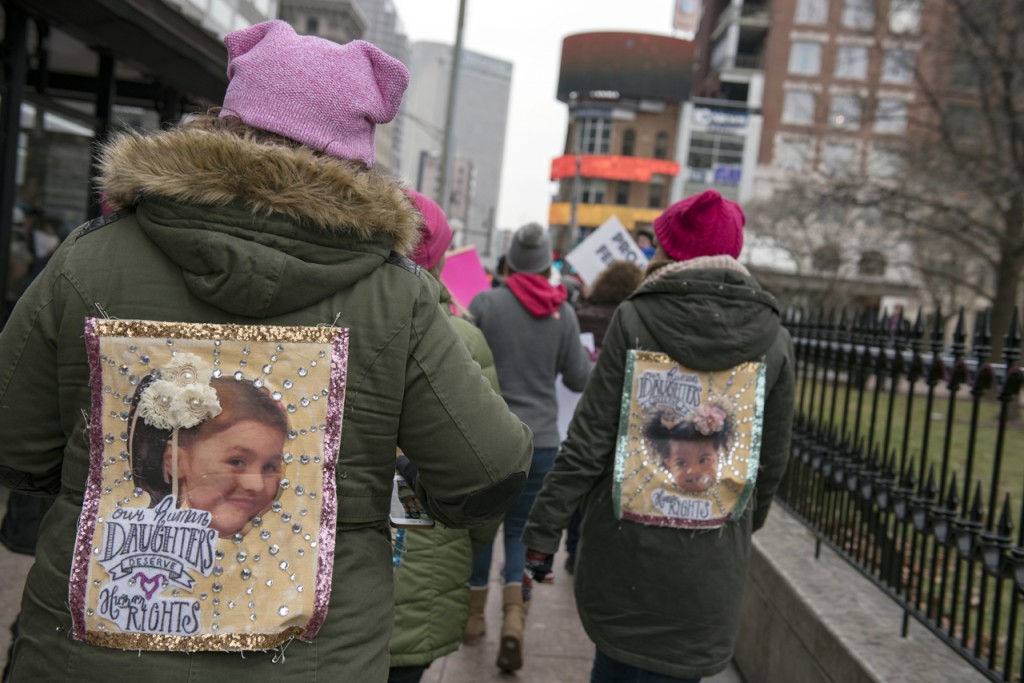Rally participants at the WMW Ohio Sister March in Columbus, Ohio wear pinned, homemade banners on their jackets as they gather in solidarity on January 15, 2017. (Margo Sabec/WOUB)
