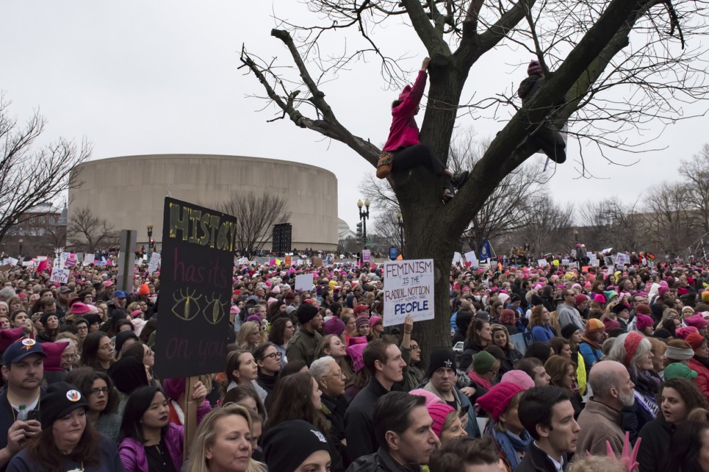 Two women climbed a tree to gain a better vantage point of the crowd and guest speakers on Saturday morning, January 21, 2017, where hundreds of thousands of participants attend the Women’s March on Washington. (Margo Sabec/WOUB)