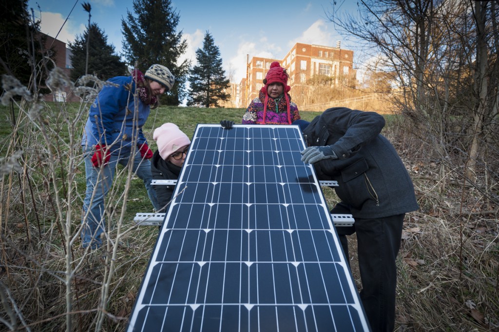 Siti Hj Abd Rahman, middle, 34, a graduate student at Ohio University, works on her masters thesis research project with her teammates and colleagues, Nora Sullivan (left), Grace Fuchs (middle-left), and Sebastian Teas (right). They have placed a solar panel that powers a device that collects data on the water quality surrounding Ohio University. (Michael Swensen/WOUB)