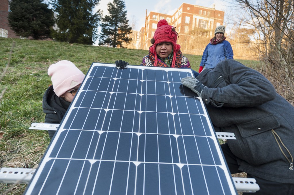 Siti Hj Abd Rahman, middle, a graduate student at Ohio University, works on her masters thesis research project with her teammates and colleagues, Nora Sullivan, background, Grace Fuchs, left, and Sebastian Teas, right. They have placed a solar panel that powers a device that collects data on the water quality surrounding Ohio University. (Michael Swensen/WOUB)