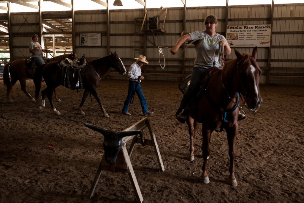 Lexy Snow (right), tosses a rope at a mock cattle as Shae Nelson (left), and Lynn Semingson (center), take their horses into the stables. (Michael Swensen/WOUB)