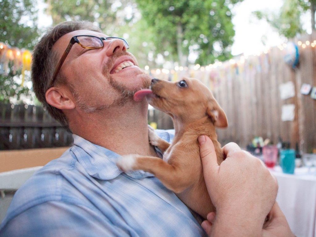 A man laughs as a puppy licks his face.