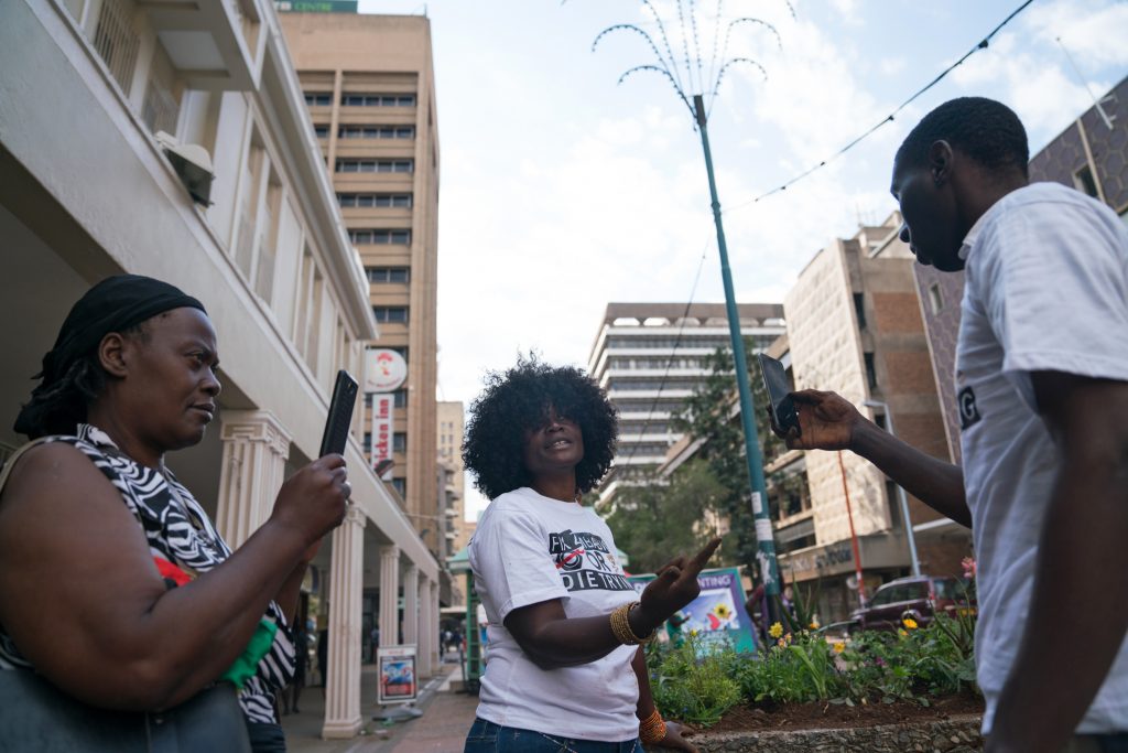 Savanna Madamombe's sister Christina (left) and Kuda Ndanga (right) record a video of Savanna while she is planting flowers in downtown Harare.