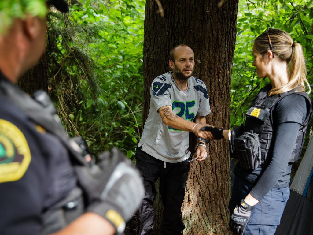 Social worker Lauren Rainbow (right) meets a man illegally camped in the woods in Snohomish County. A new program in the county helps people with addiction, instead of arresting them.