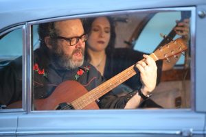 man playing guitar in back seat of 1960s car