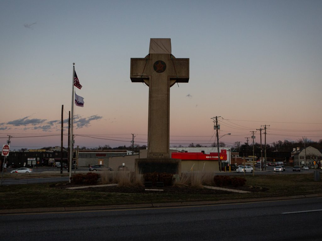 The cross sits in the median at a busy five-way intersection.