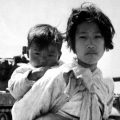With her brother on her back a war weary Korean girl tiredly trudges by a stalled M-26 tank, at Haengju, Korea, 6/9/51.