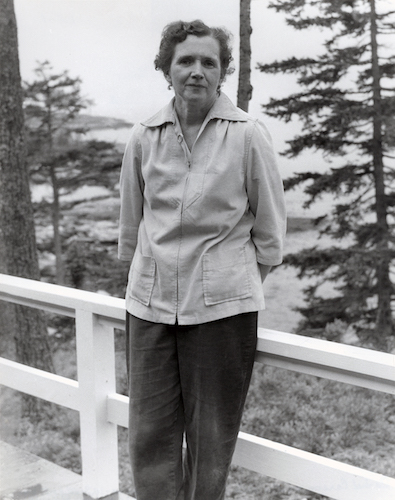 Rachel Carson in long shirt and slacks leaning against a waist high white fence