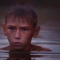 young boy swimming in pond in water up to his neck