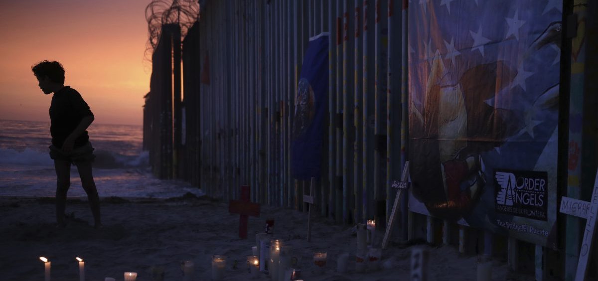 A youth in Tijuana, Mexico, stands by the border fence that separates Mexico from the United States, where candles and crosses stand in memory of migrants who have died during their journey toward the U.S.