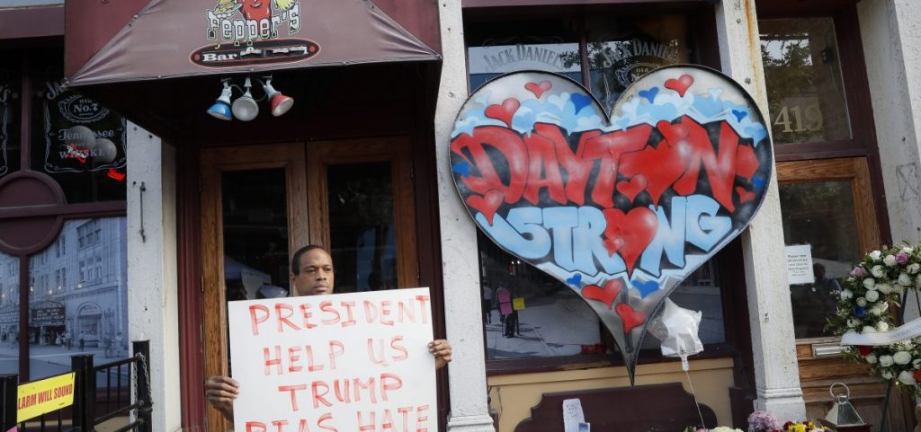 Damon Smith presents a message to President Donald Trump beside a makeshift memorial for the slain and injured victims of a mass shooting that occurred in the Oregon District on Aug. 7, 2019, in Dayton, Ohio.  Twenty-four-year-old Connor Betts opened fire in Dayton early Sunday, killing several people including his sister, before officers fatally shot him. (AP Photo | John Minchillo)