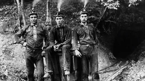three coal miners sitting on coal cart posing for picture