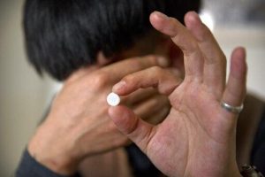 A person holds up a white pill to the camera. The person hides their fade in shame that the pills are addictive.