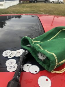 A green felt Crown Royal bag with number tags on top of a red car