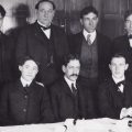 group of men in suits seated at table facing camera, early 190ss