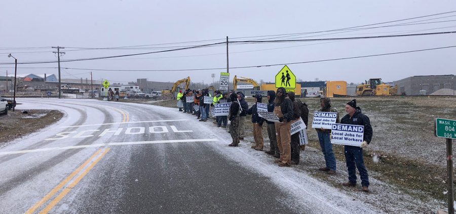 Workers with picket lines on the side of country road. There is a dusty of snow on the road