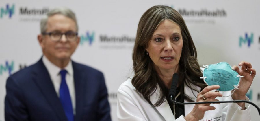 Ohio Department of Health Director Amy Acton holds up a mask as she gives an update at MetroHealth Medical Center Thursday, Feb. 27, 2020, in Cleveland, on the state's preparedness and education efforts to limit the potential spread of a new virus which caused a disease called COVID-19. Ohio Governor Mike DeWine, left, watches.