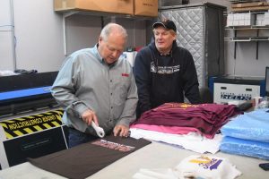 Dave Kasler, left, and Dr. Tim LaVelle, right. Kasler is cutting a t-shirt for use in making protective cloth masks. 