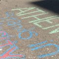 Mary Nally writes "Athens Stands in Solidarity" with chalk on the sidewalk outside of the Athens County Courthouse on Sunday, May 31, 2020.