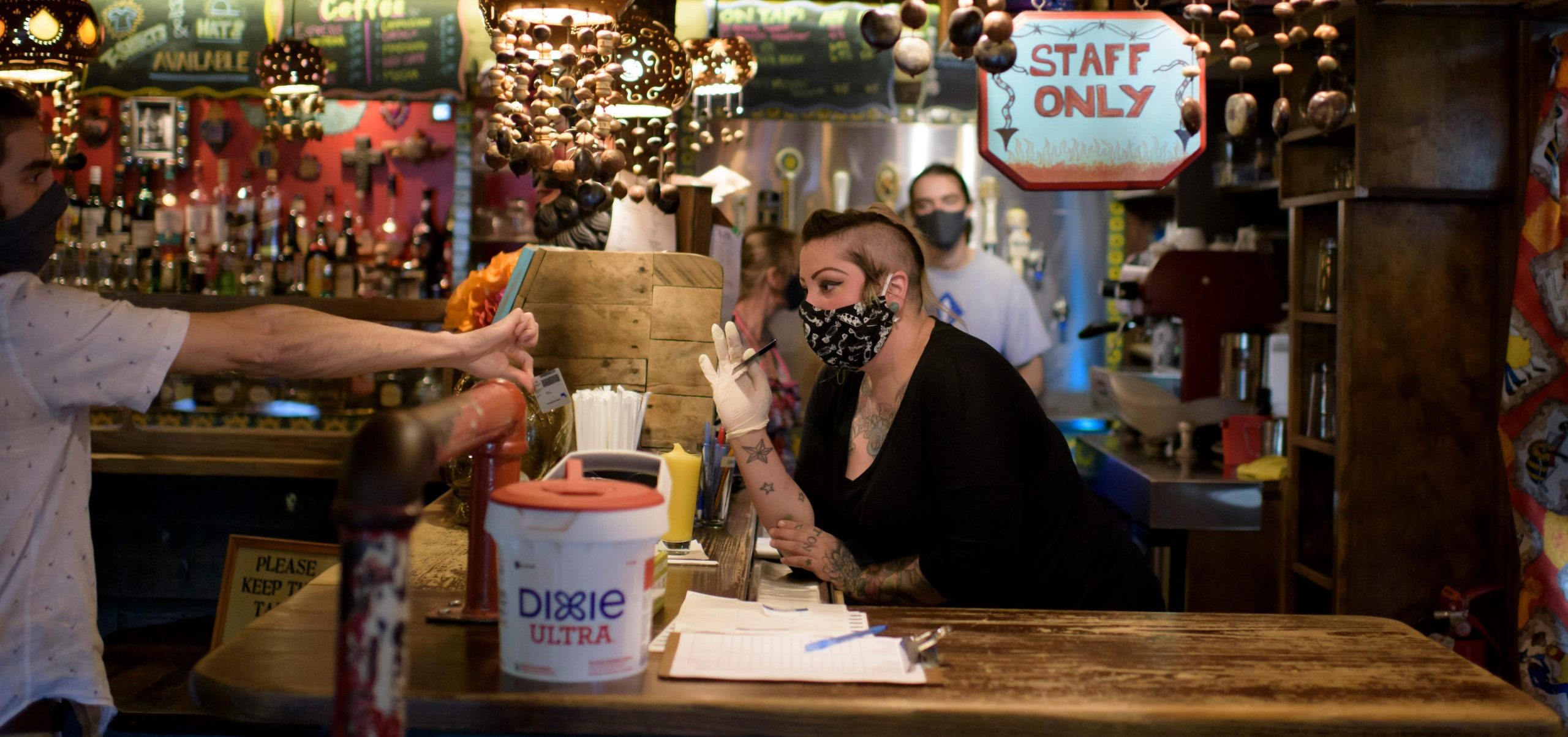 A bartender wearing a face mask and gloves checks a patron's ID at Under the Volcano in Houston last month. Texas is one of the states seeing a big uptick in coronavirus cases and hospitalizations.