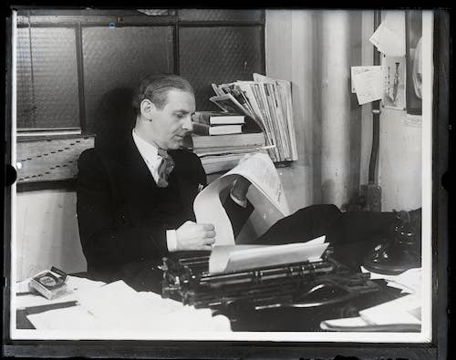 Winchell reads a long paper at his desk in the Daily Mirror office.