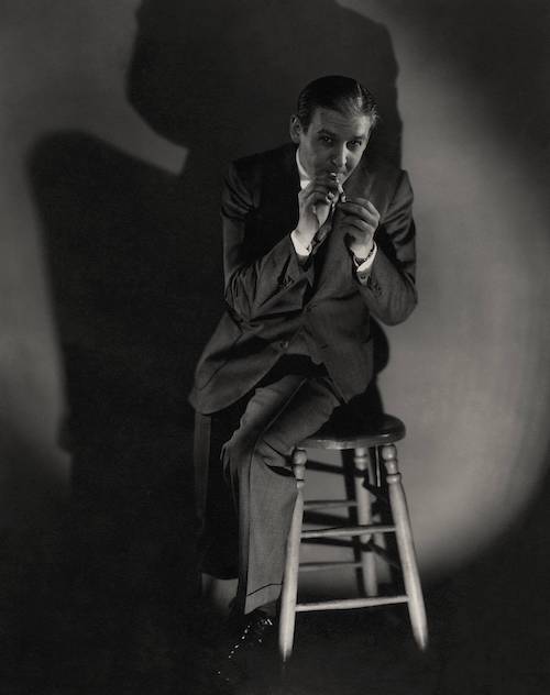 Young Winchell sits on a stool and lights a cigarette.