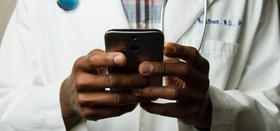 A doctor holds a phone, presumably for a telemedicine visit