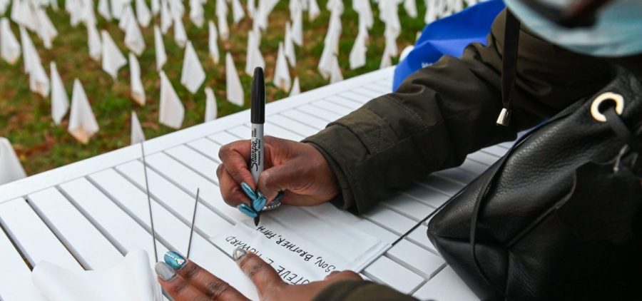Patrice Howard writes on white flags before planting them to remember her recently deceased father and close friends in November at "IN AMERICA How Could This Happen...," a public art installation in Washington, D.C. Led by artist Suzanne Firstenberg, volunteers planted white flags in a field to symbolize each life lost to COVID-19 in the U.S.