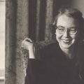 Black and white of Flannery O’Connor in front of window