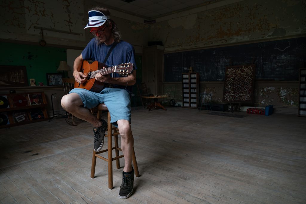 Brian Smith, a resident artist at the Pioneer School Community Arts Center, plays guitar for a portrait in one of his two rooms he rents for his art work, in Zanesville, Ohio, on Wednesday, June 9, 2021. "This has been my dream for 30 years, to be in this school and to be working and recording musicians and to help people feel comfortable," said Smith. This space, called the Christmas Tree room, has been named and designed by Smith. Smith's plan is to eventually clear coat the room to help preserve the layers of the school's history while the space is being lived in.