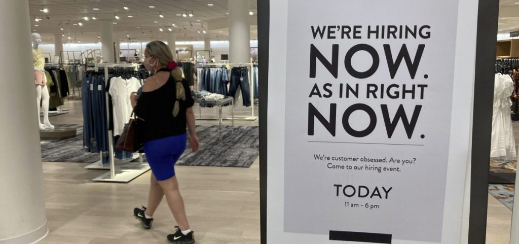 A customer walks behind a sign at a Nordstrom store seeking employees on May 21, in Coral Gables, Fla. Citing a severe shortage of workers, half of the nation's governors have decided to end extra federal jobless benefits months early.