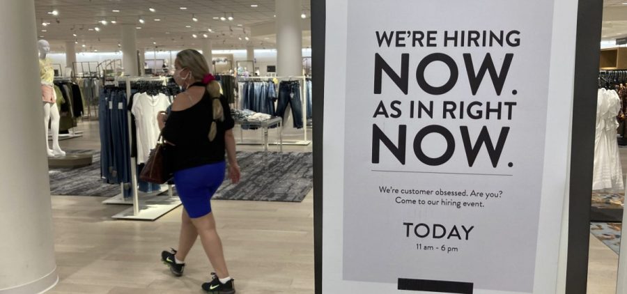 A customer walks behind a sign at a Nordstrom store seeking employees on May 21, in Coral Gables, Fla. Citing a severe shortage of workers, half of the nation's governors have decided to end extra federal jobless benefits months early.