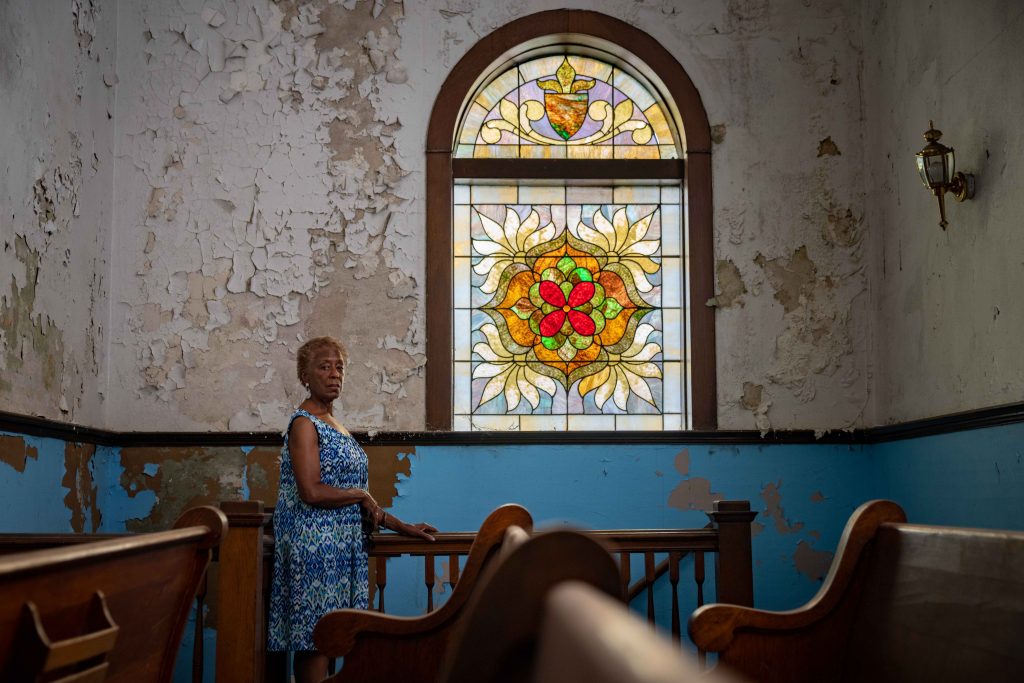 Dr. Tee Ford-Ahmed, director of communications for the Mount Zion Baptist Church Preservation Society, stands inside the church next to a stained glass window that has since become the symbol for restoring the church.