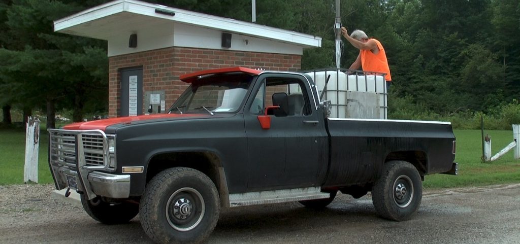 A man pours water from a water dispensary into the back of his truck