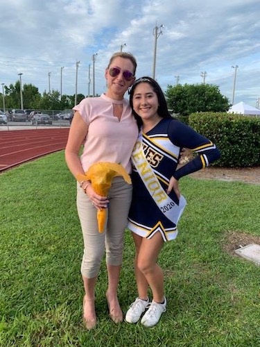 A mom standing next to her jigh school seniots cheerleader