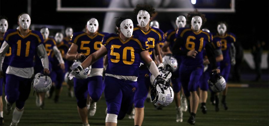 Bloom-Carroll players wearing halloween masks run through the tunnel and onto the field