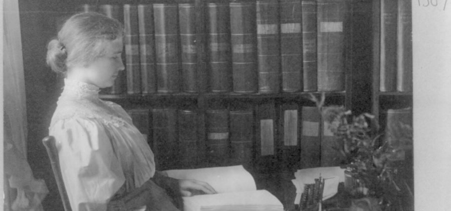 Black and white image of Helen Keller reading using her hands in a library. Credit: Courtesy of Library of Congress