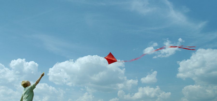woman flying red kite in beautiful blue sky with puffy clouds