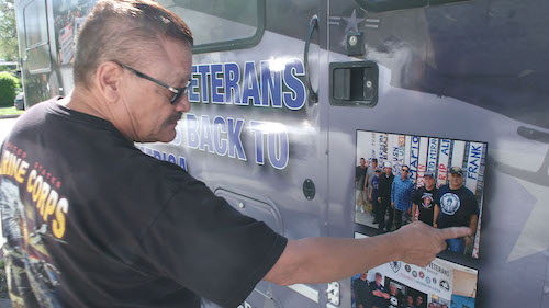 Manuel Valenzuela pointing out photos of deported veterans on the side of his RV.