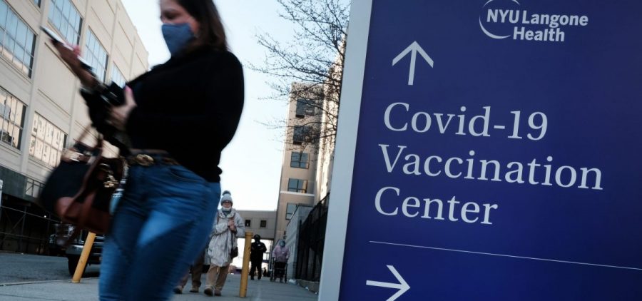 People walk by a sign for both a COVID-19 testing clinic and a Covid vaccination location outside of a Brooklyn, New York, hospital on March, 29 2021.