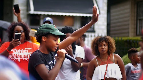 woman with hand raised speaking to crowd