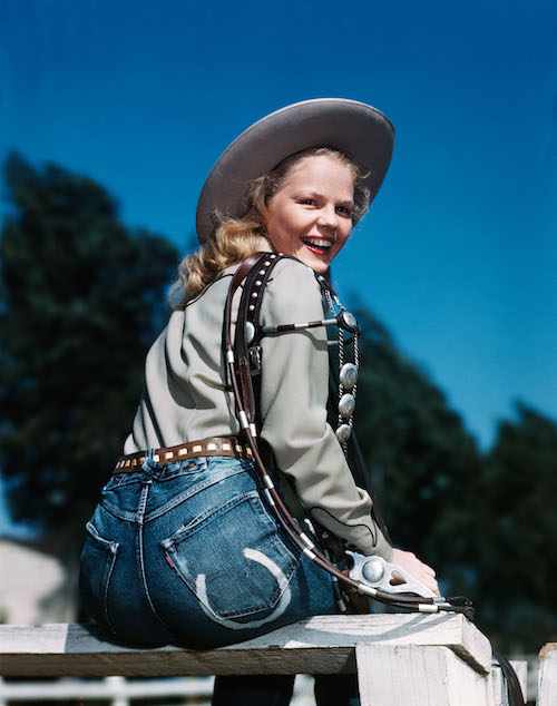 1940s-50s SMILING BLOND WOMAN WEARING WESTERN COWGIRL CLOTHES LOOKING OVER SHOULDER SITTING ON WOODEN FENCE